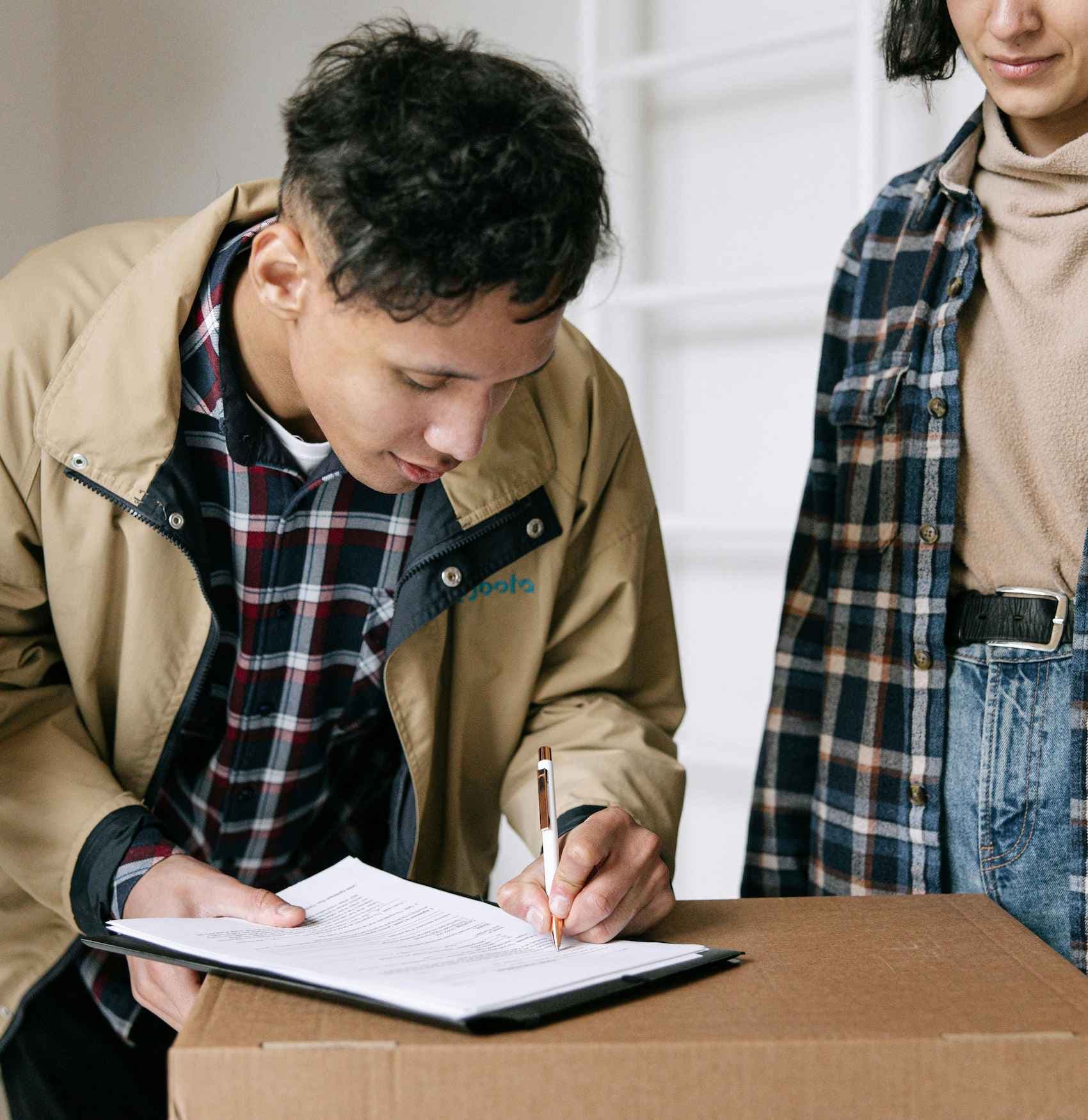 Un jeune homme en train de signer un contrat avec une dame en arrière plan